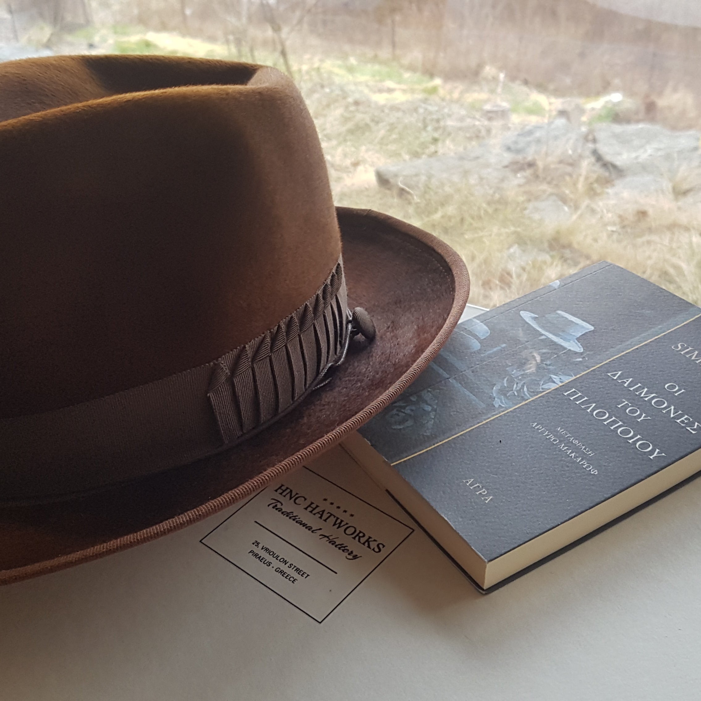 A stylish brown felt fedora hat placed next to a book on a wooden table, evoking a sense of timeless fashion and craftsmanship.