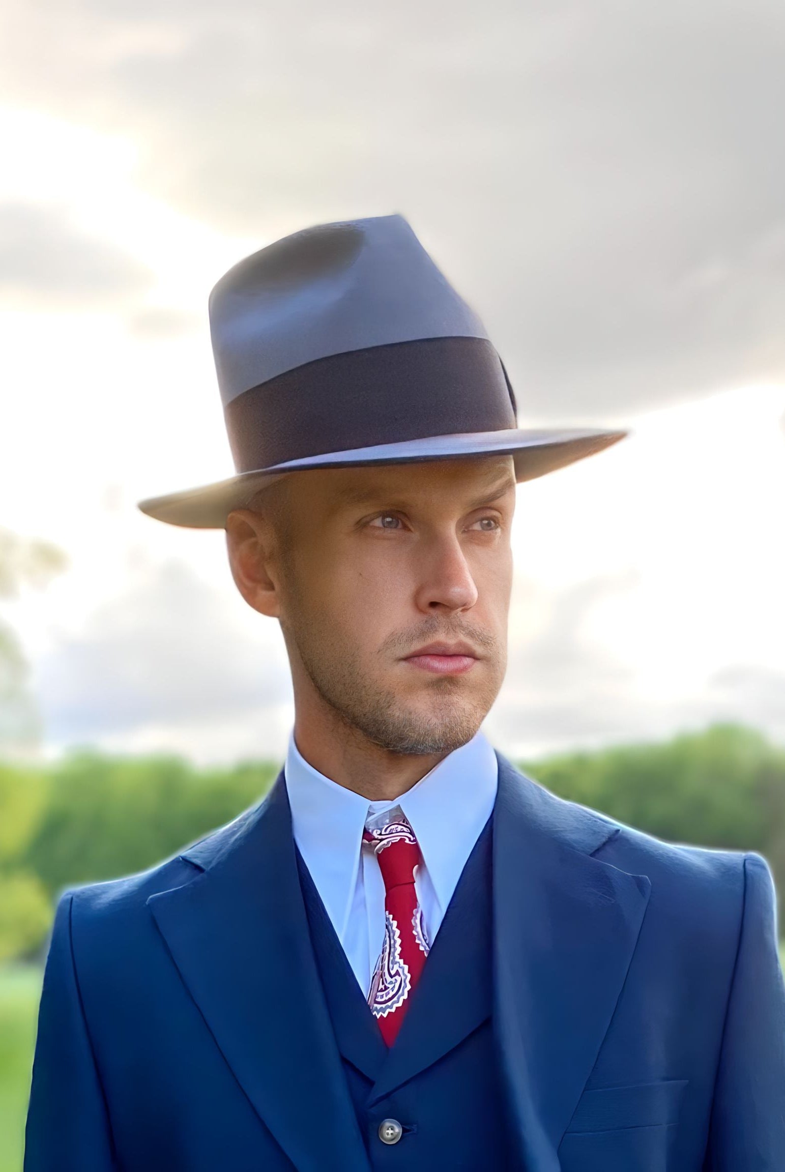 A discerning man in a custom beaver felt fedora hat, exuding sophistication and a unique personal style against a vibrant natural backdrop.