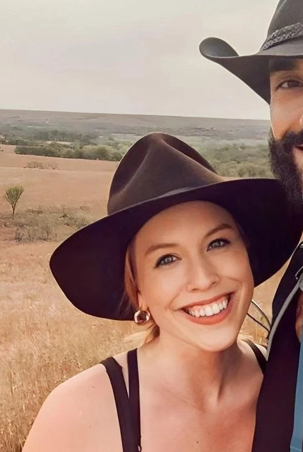 A couple happily explores a scenic open field, both stylishly wearing Agnoulita's country hats, perfect for outdoor adventures