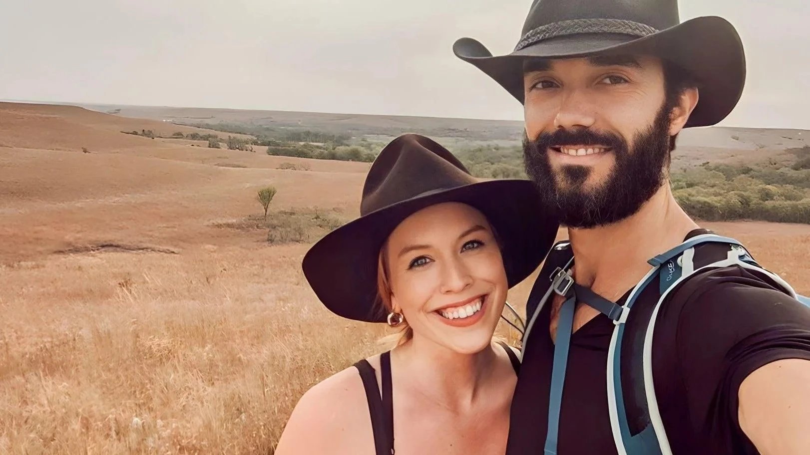 A couple happily explores a scenic open field, both stylishly wearing Agnoulita's country hats, perfect for outdoor adventures