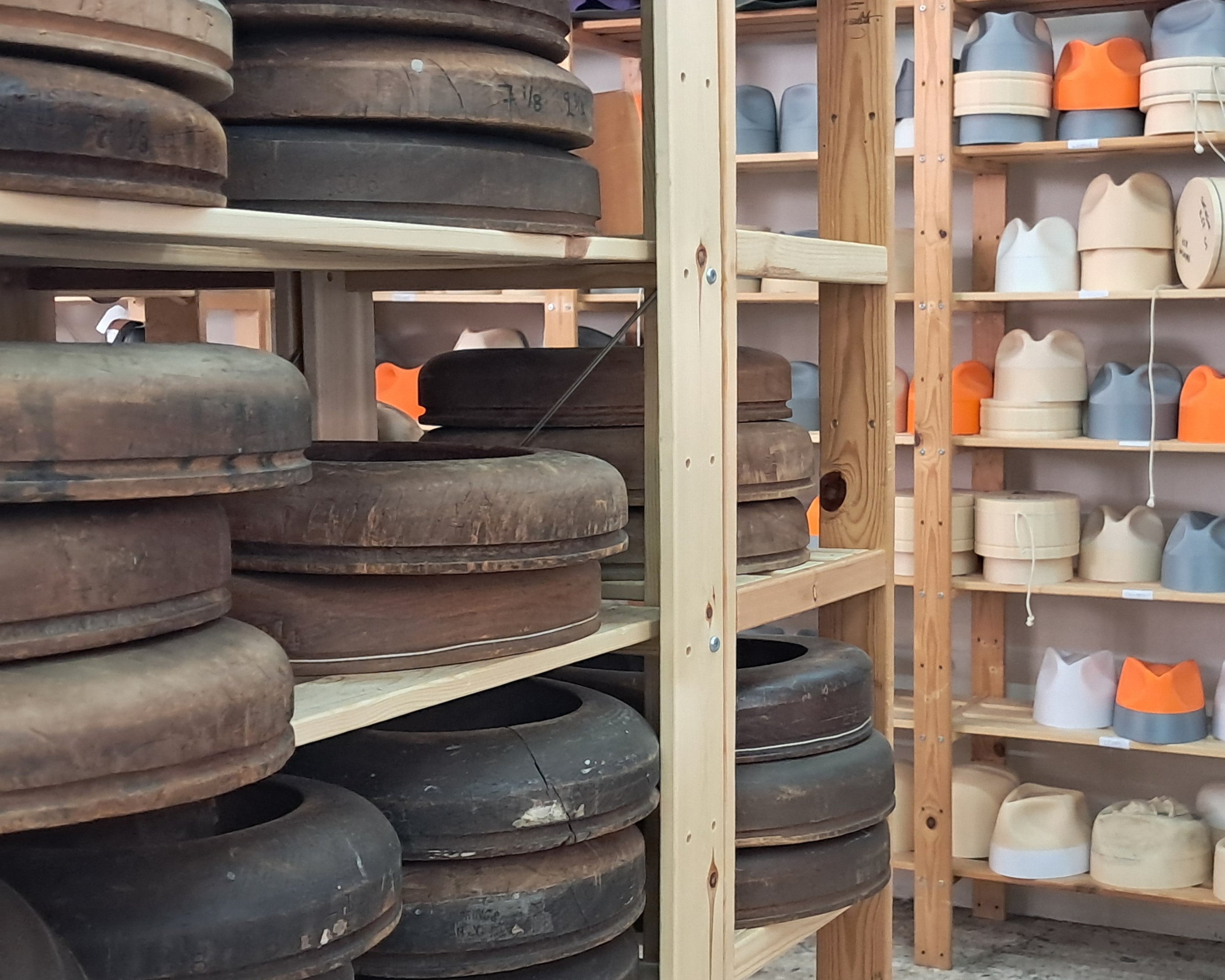 Shelves with hat brim flanges on the left and 3d printed hat blocks on the right in a hat workshop setting.