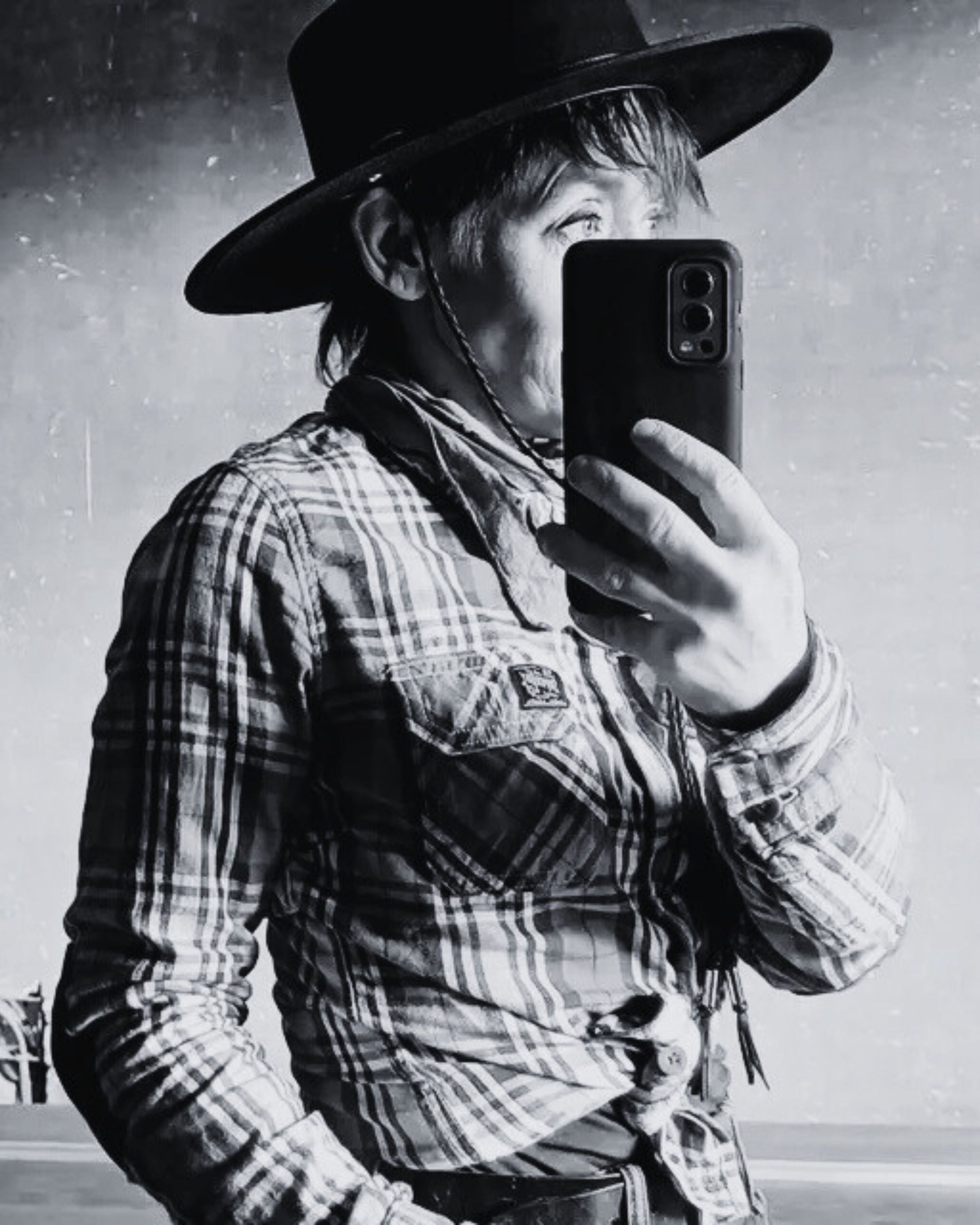 Person wearing a cowboy hat and plaid shirt taking a mirror selfie.