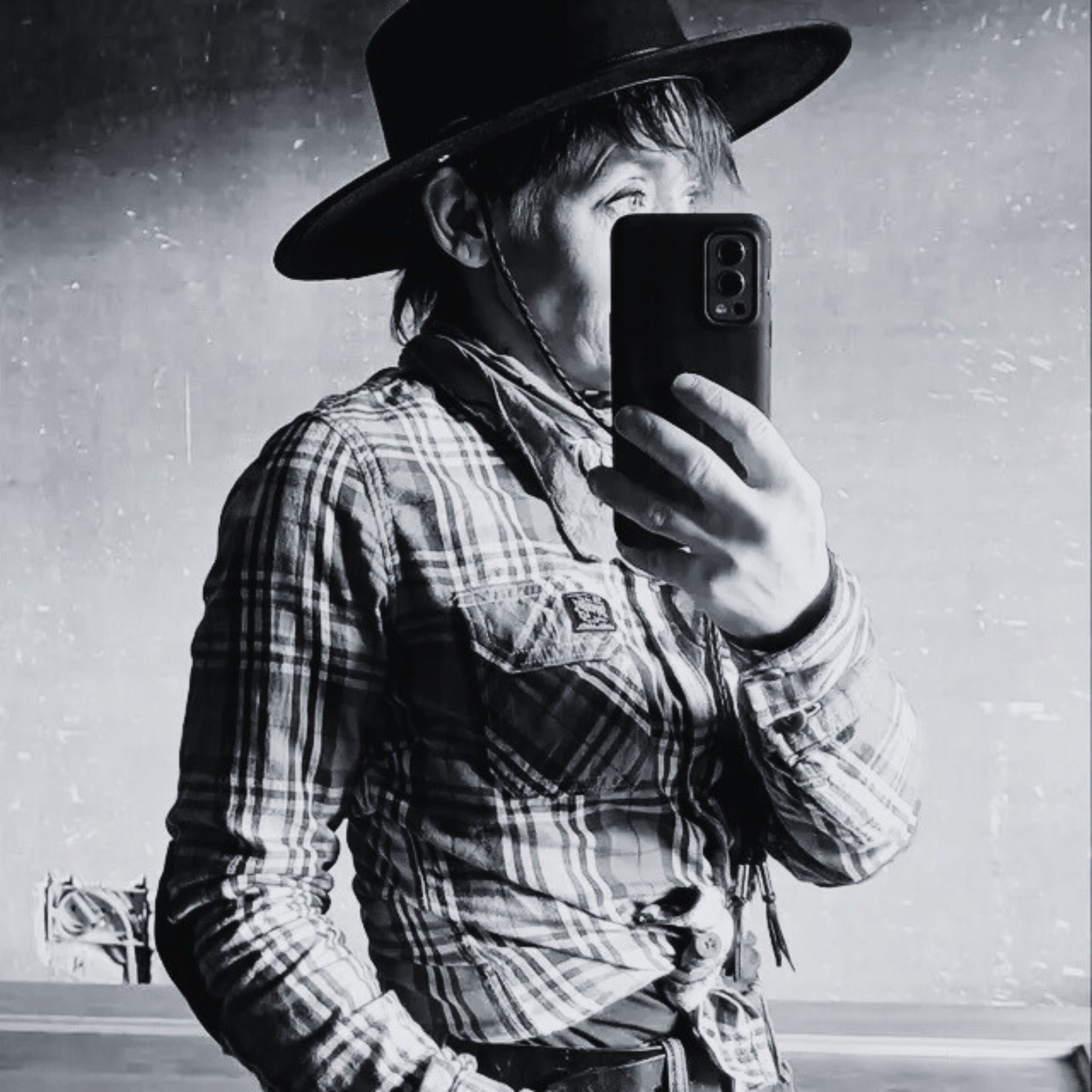 Person wearing a cowboy hat and plaid shirt taking a mirror selfie.