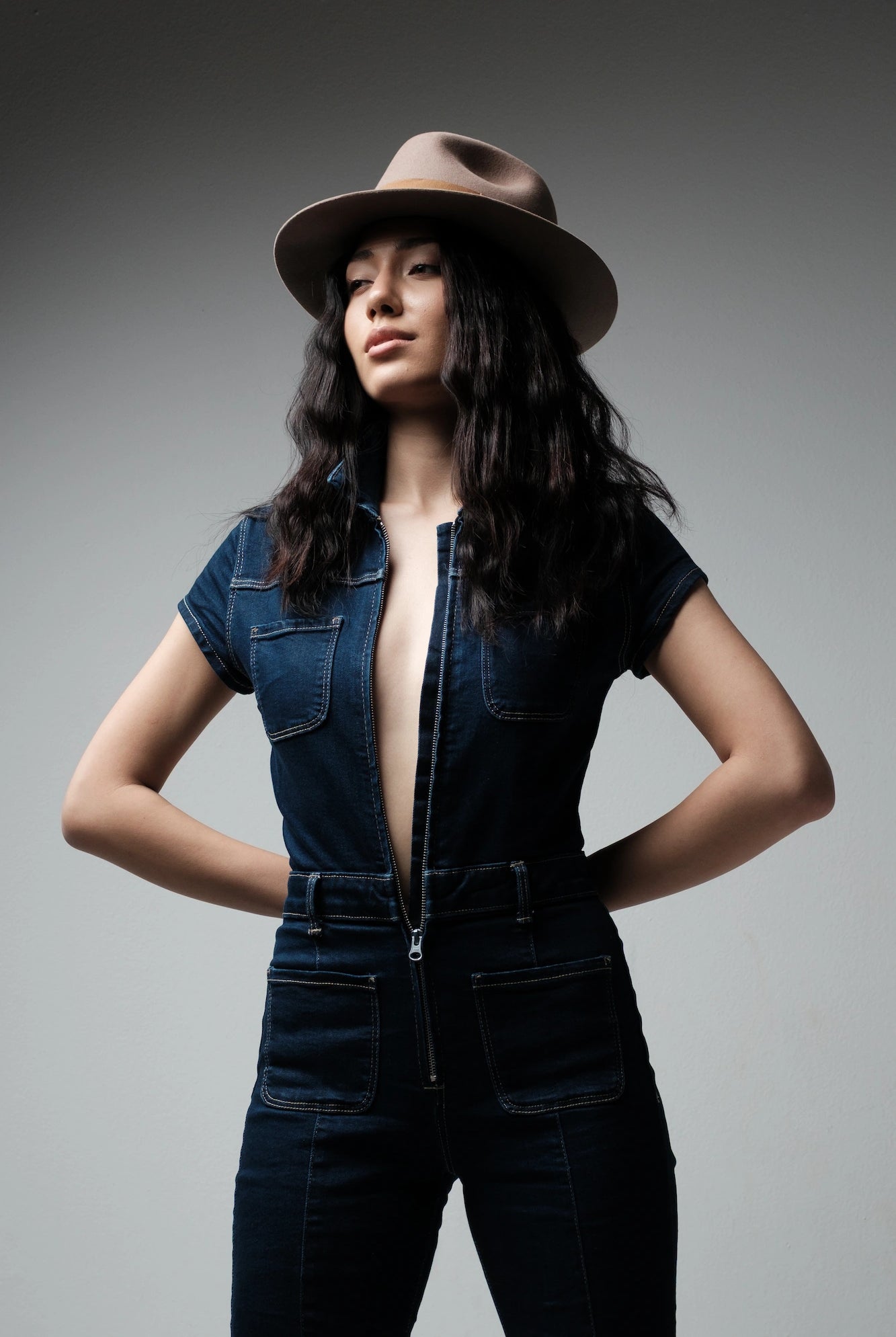 Woman wearing a denim outfit and brown hat against a gray background