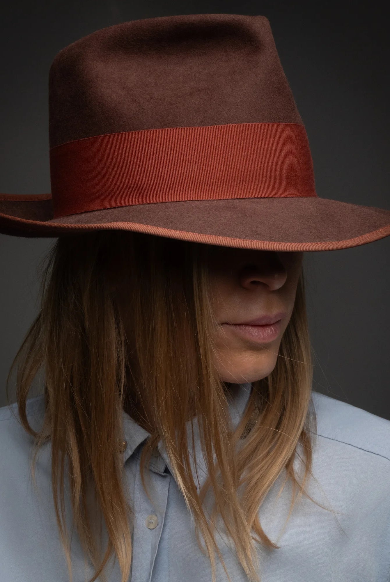 Person wearing a brown hat with a red band against a dark background