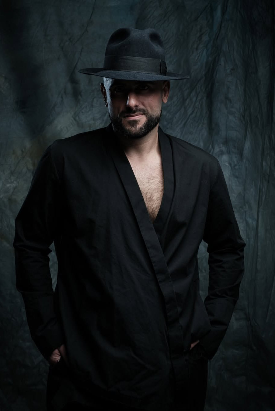 Man wearing a black hat and black outfit against a dark textured background