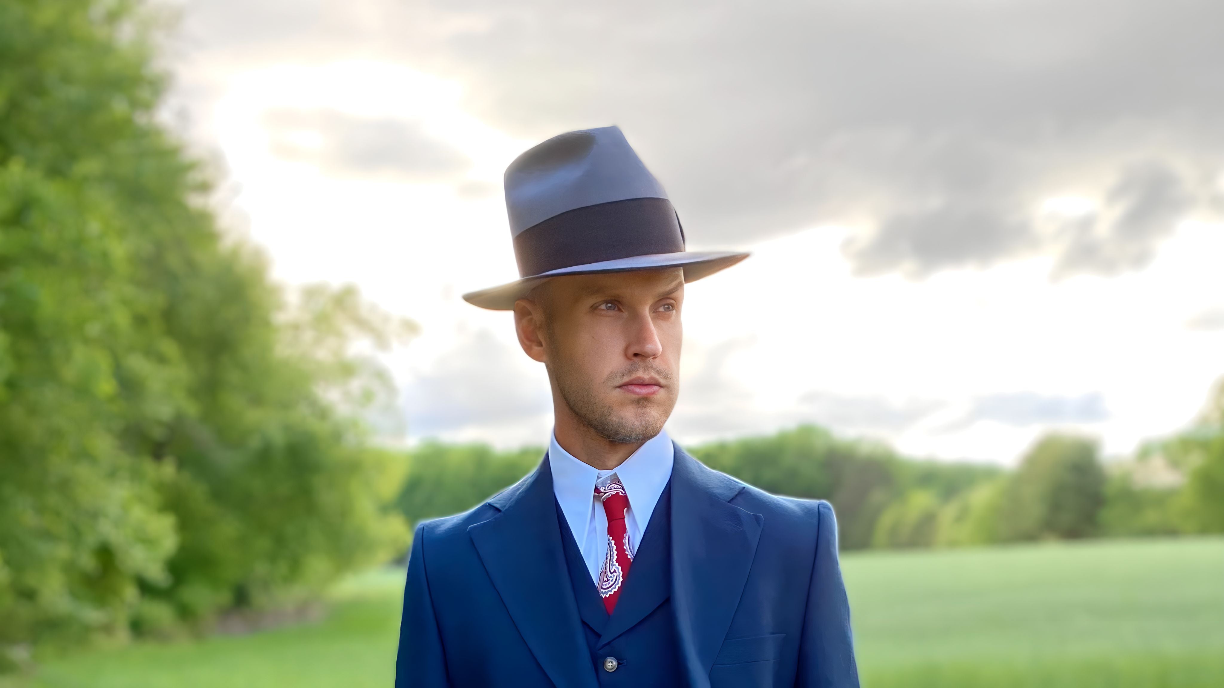 A discerning man in a custom beaver felt fedora hat, exuding sophistication and a unique personal style against a vibrant natural backdrop.