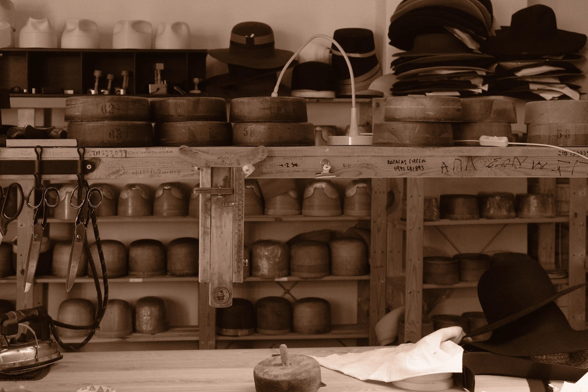 Agnoulita Hats workshop in Athens, showing traditional wooden hat blocks, handcrafted felt hats, measuring tools, scissors, and workbench.