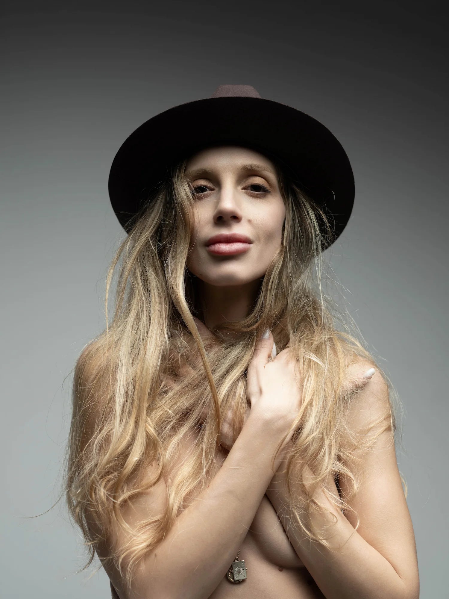 Naked woman wearing a black hat against a gray background