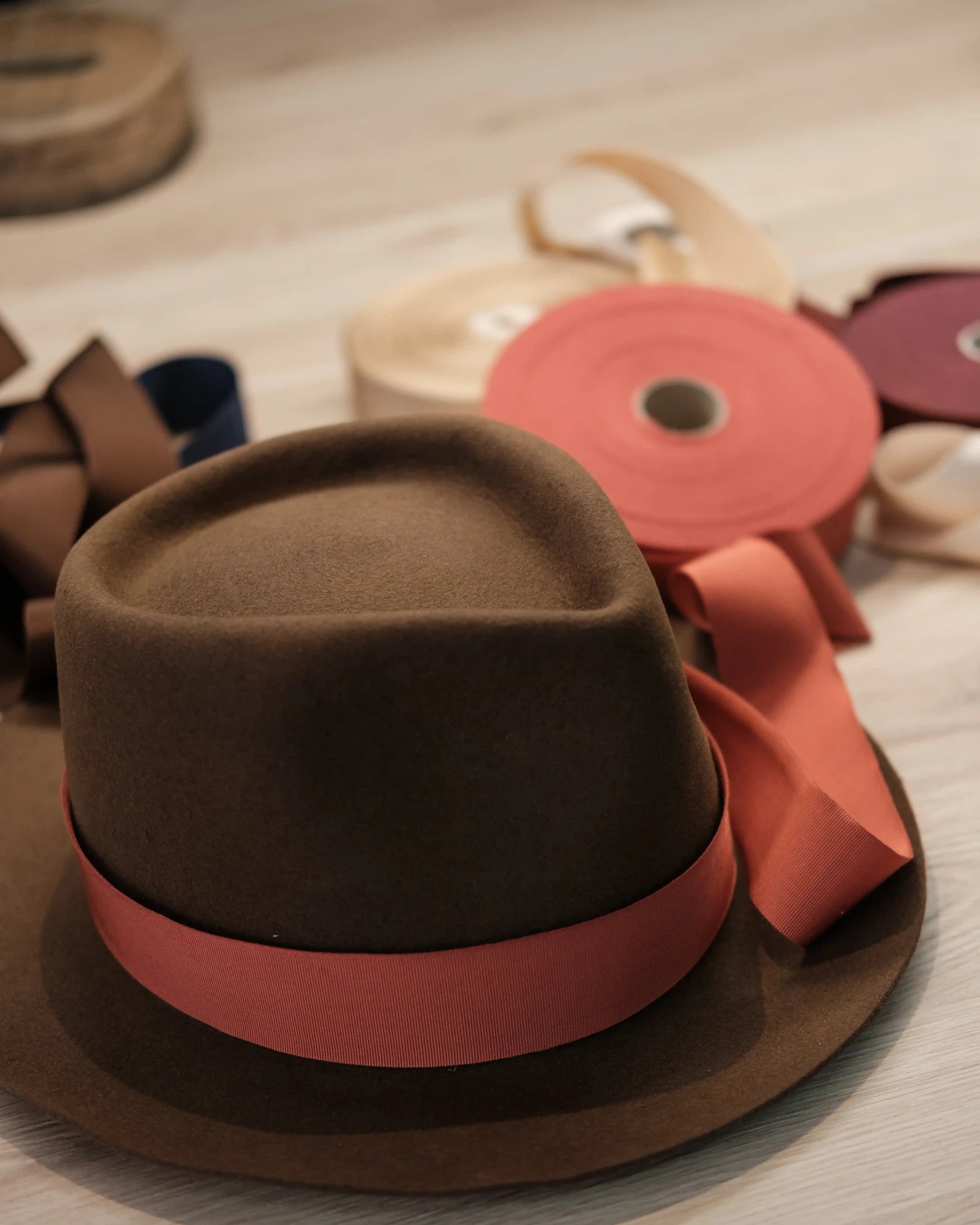 Brown fedora hat with a red band on a wooden surface with ribbons.