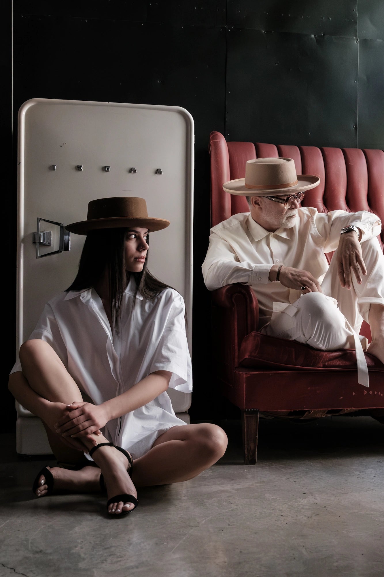 Two people in vintage attire sitting in a room with a red couch.
