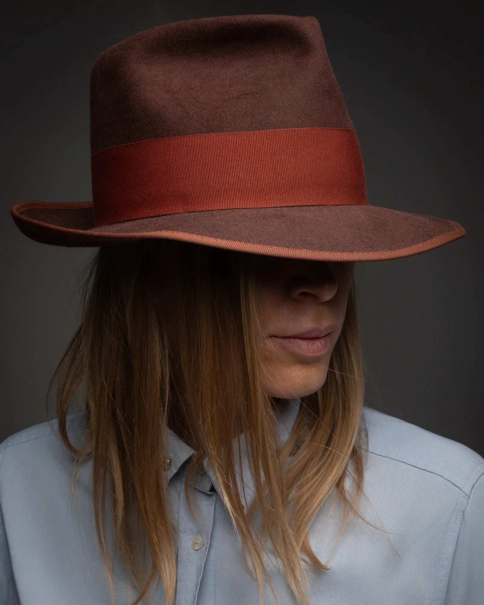 Person wearing a brown hat with a red band against a dark background