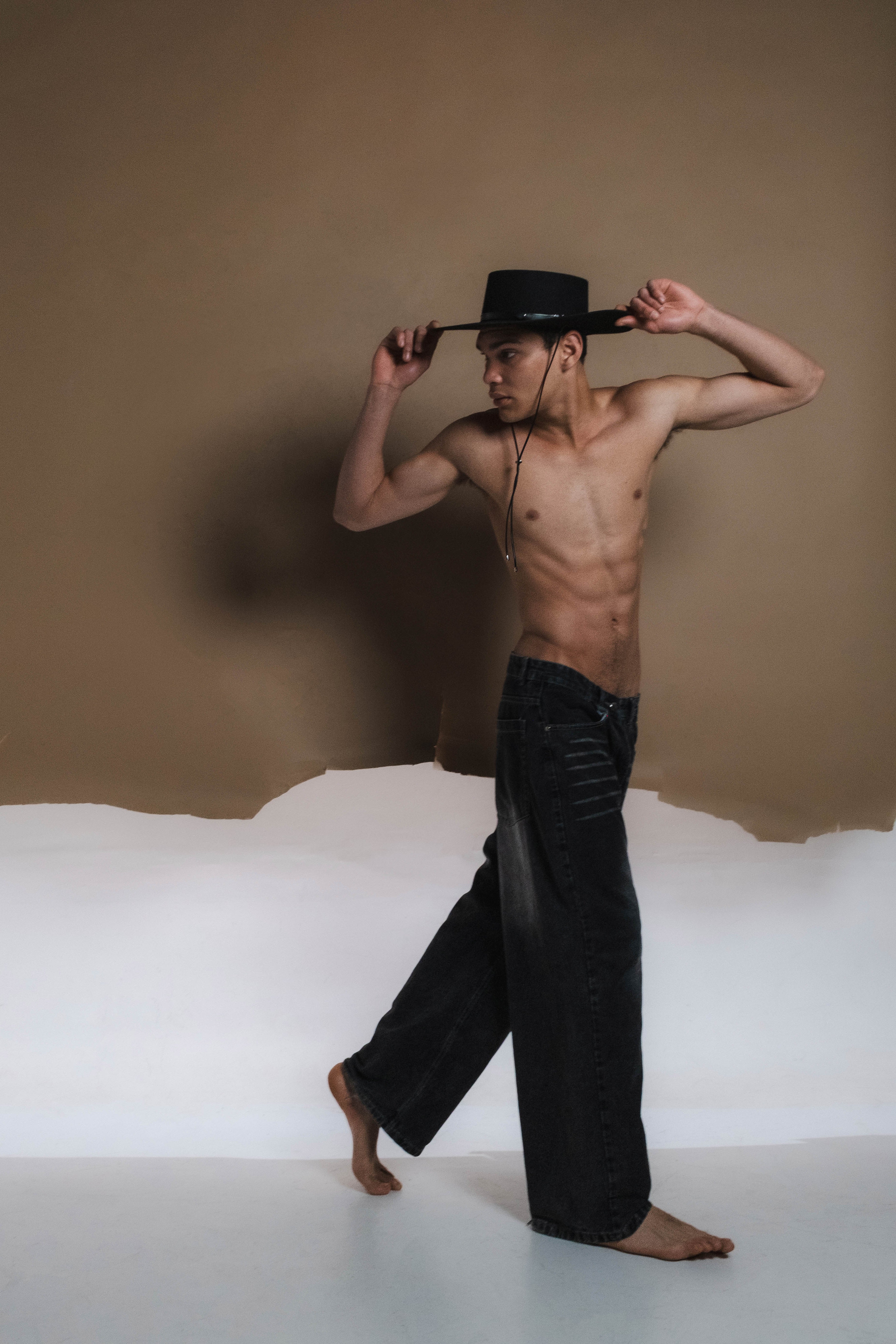 Man wearing black leather pants and a top hat against a neutral background