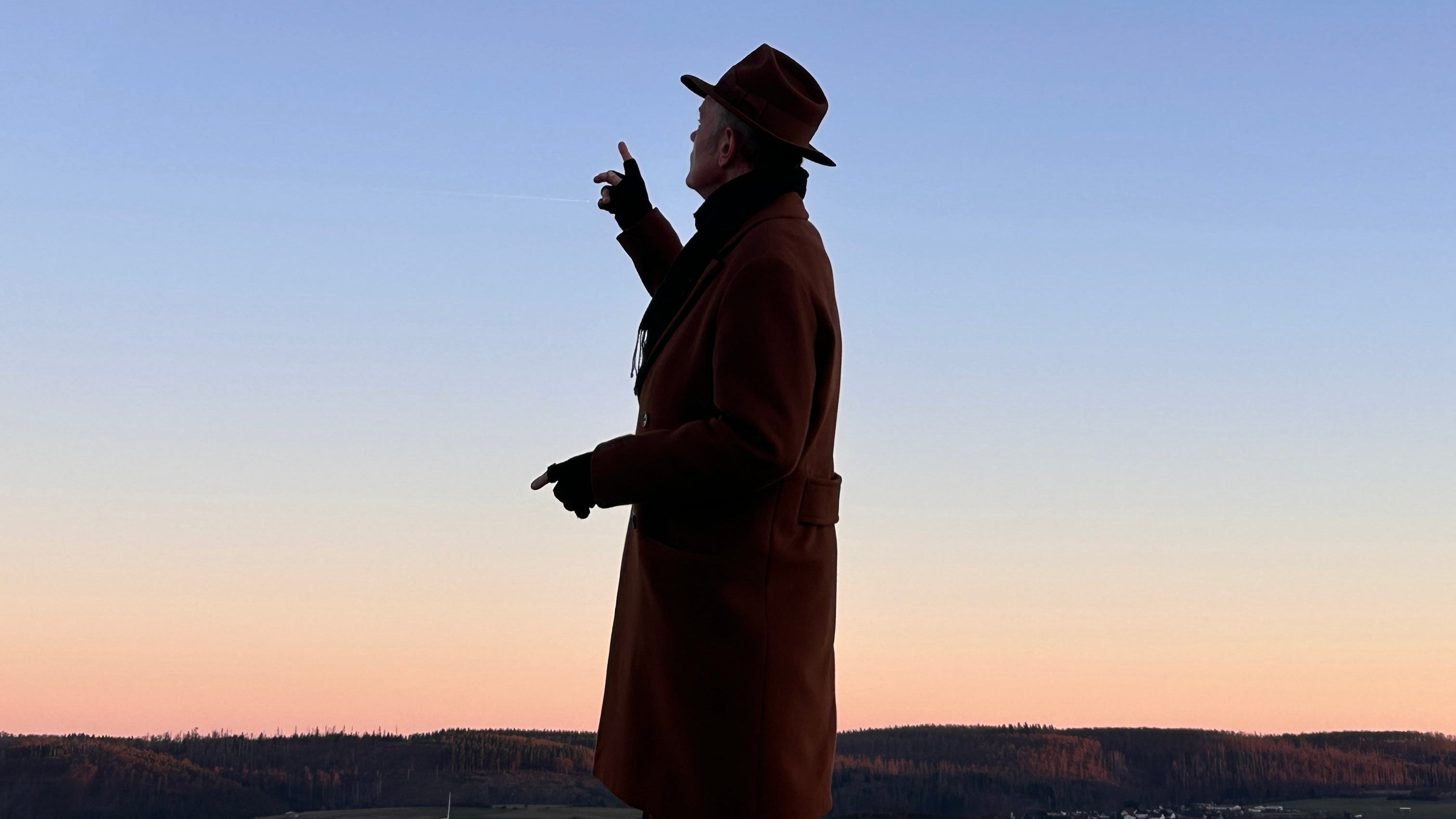 Silhouette of a person against a blue sky with a contrail and moon.