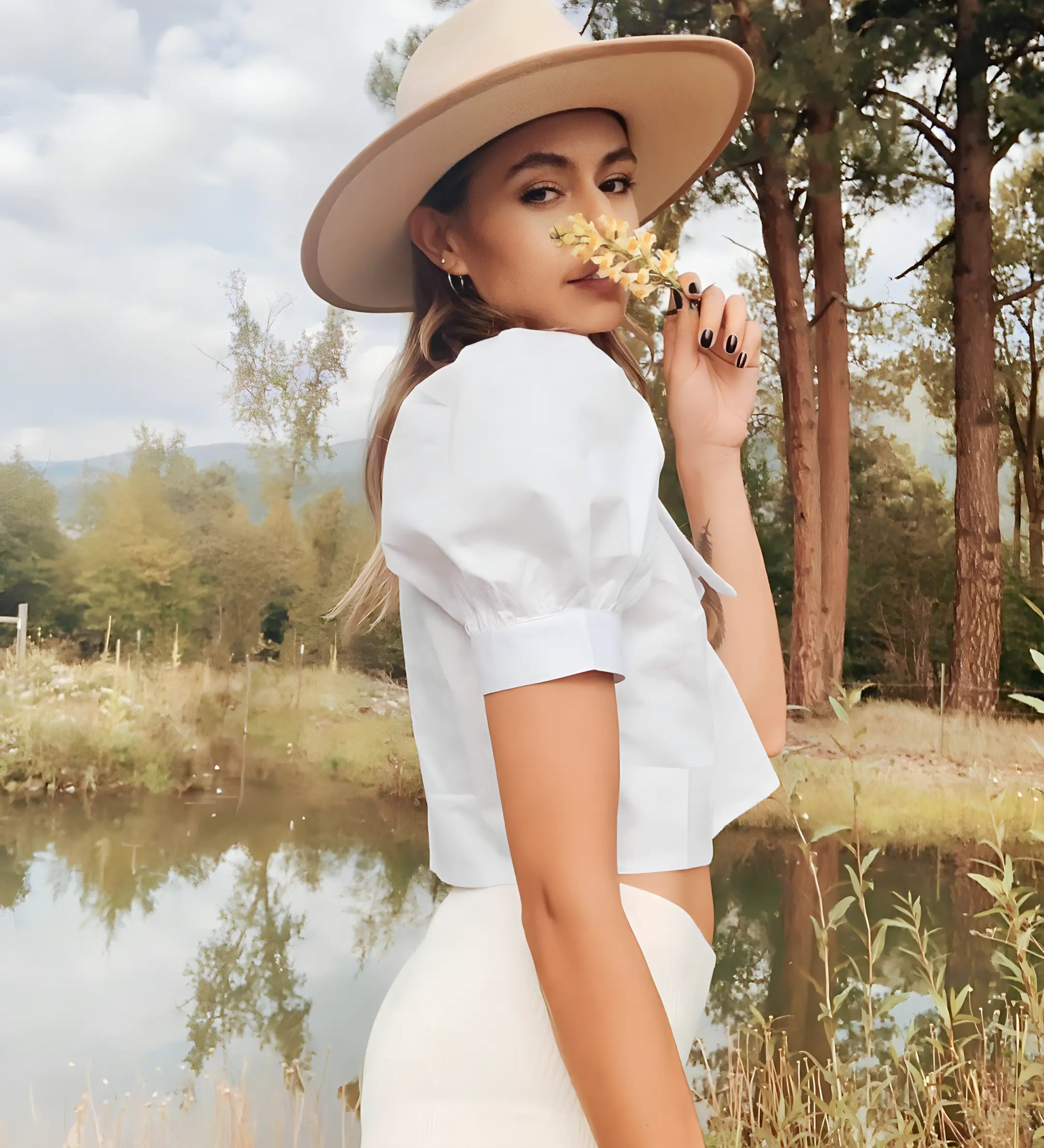 Lakeside photo of a young woman smelling a flower, wearing her Agnoulita wide brim fedora