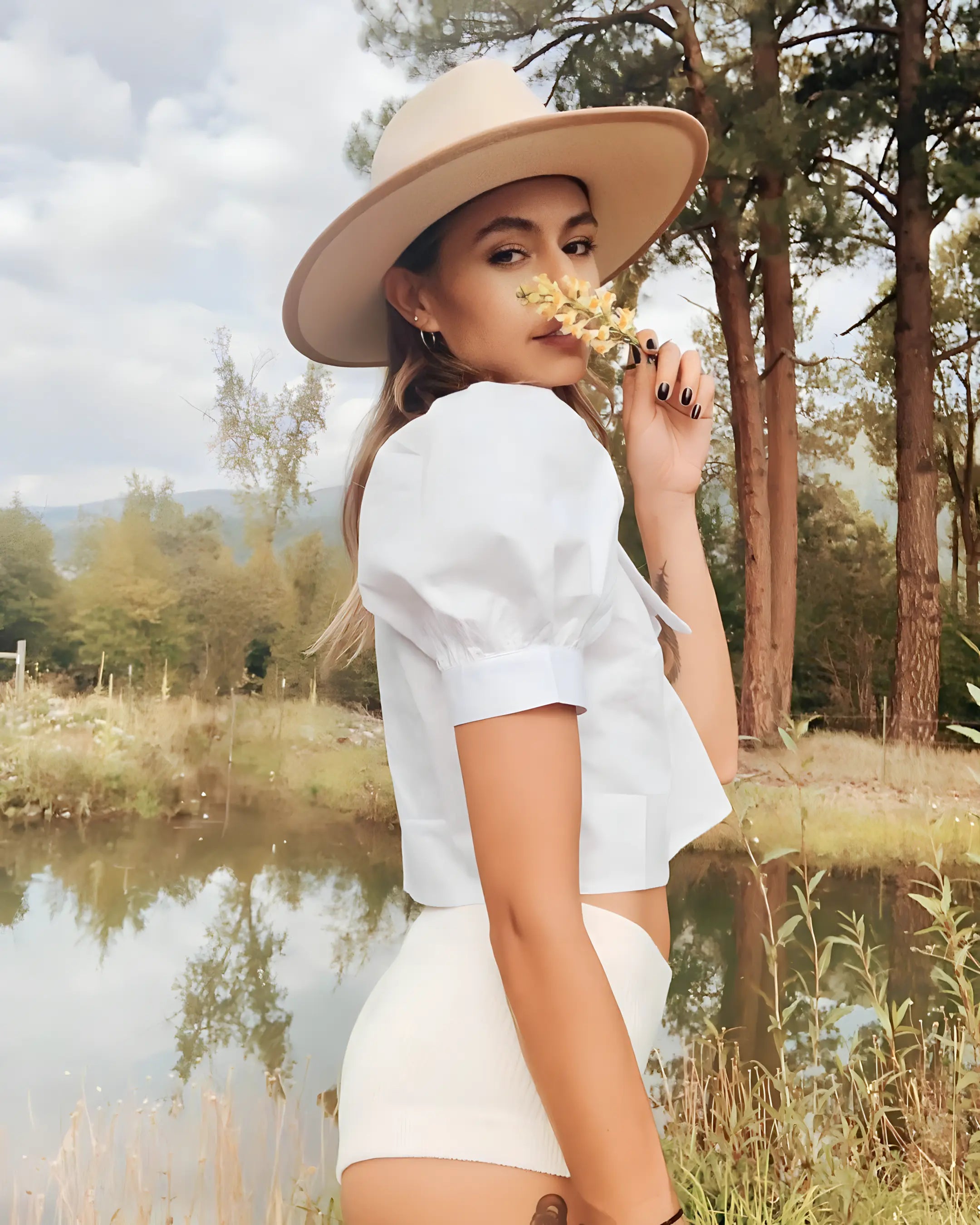 Lakeside photo of a young woman smelling a flower, wearing her Agnoulita wide brim fedora