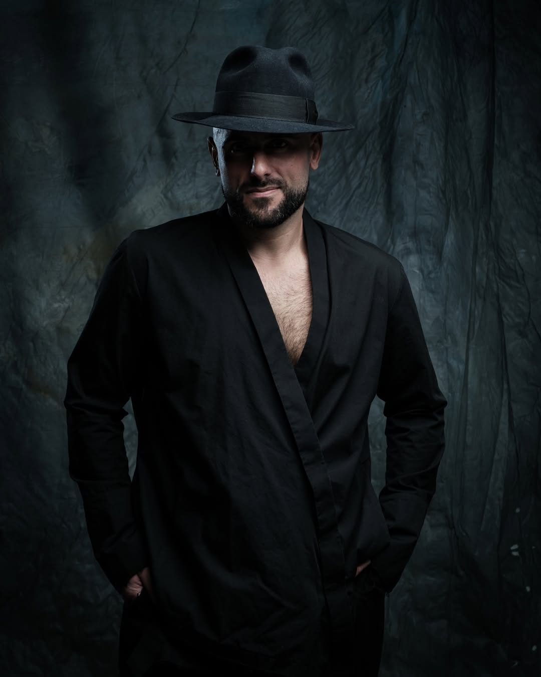 Man wearing a black hat and black outfit against a dark textured background