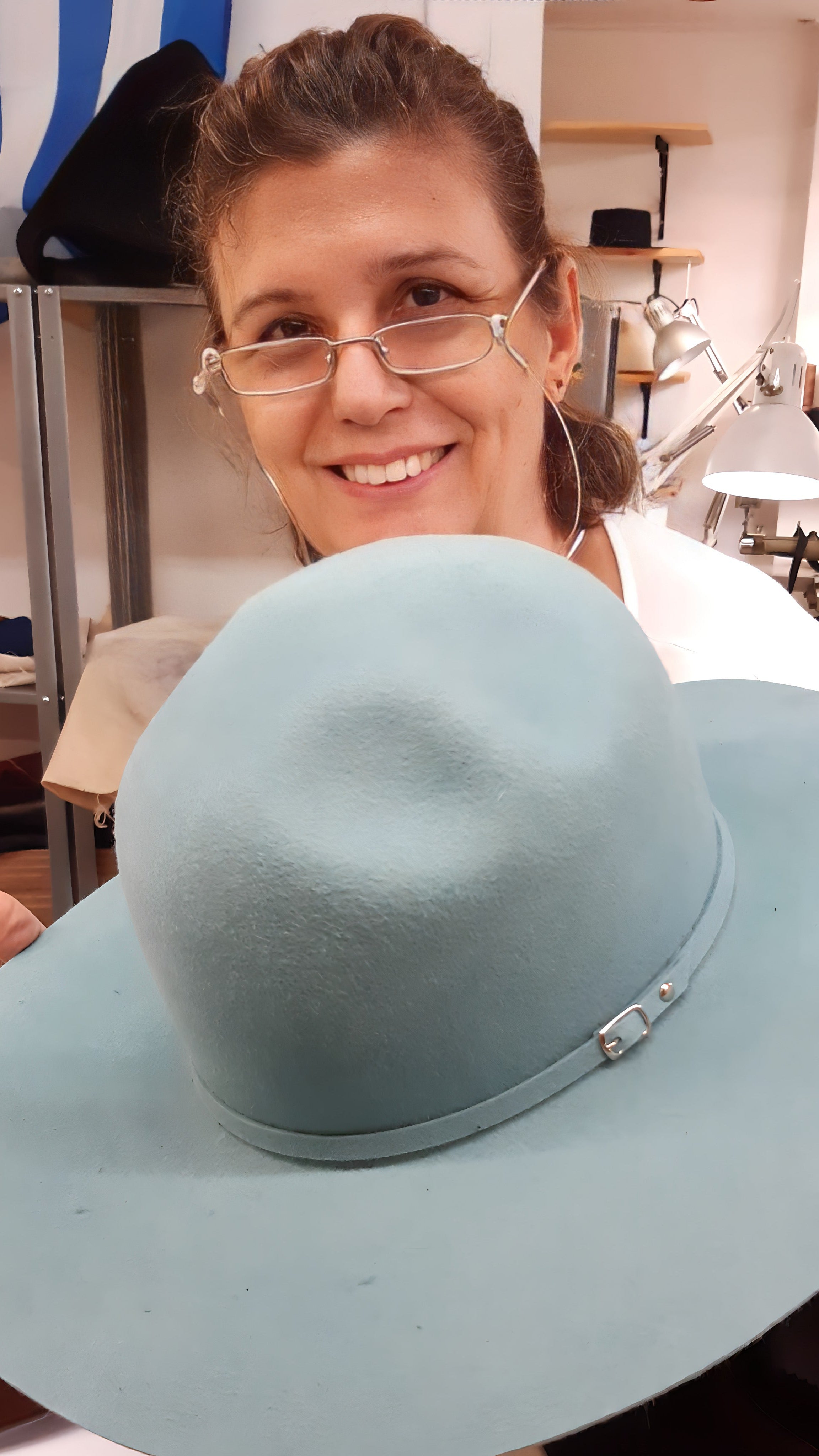 Woman holding a light blue wide-brimmed hat in an indoor setting