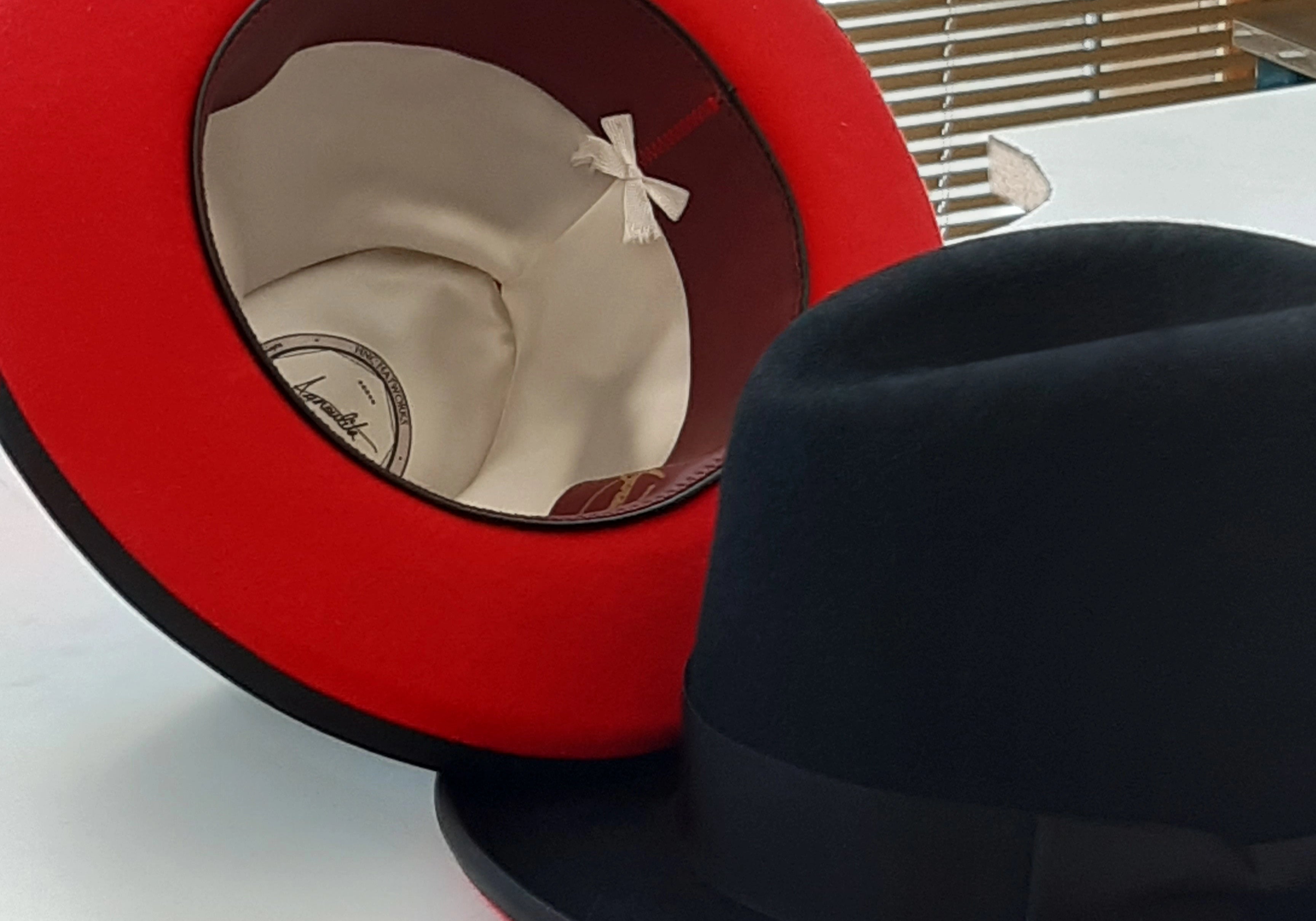 Bench photo of two double-tone Agnoulita Onyx fedoras with black tops and red under brims.